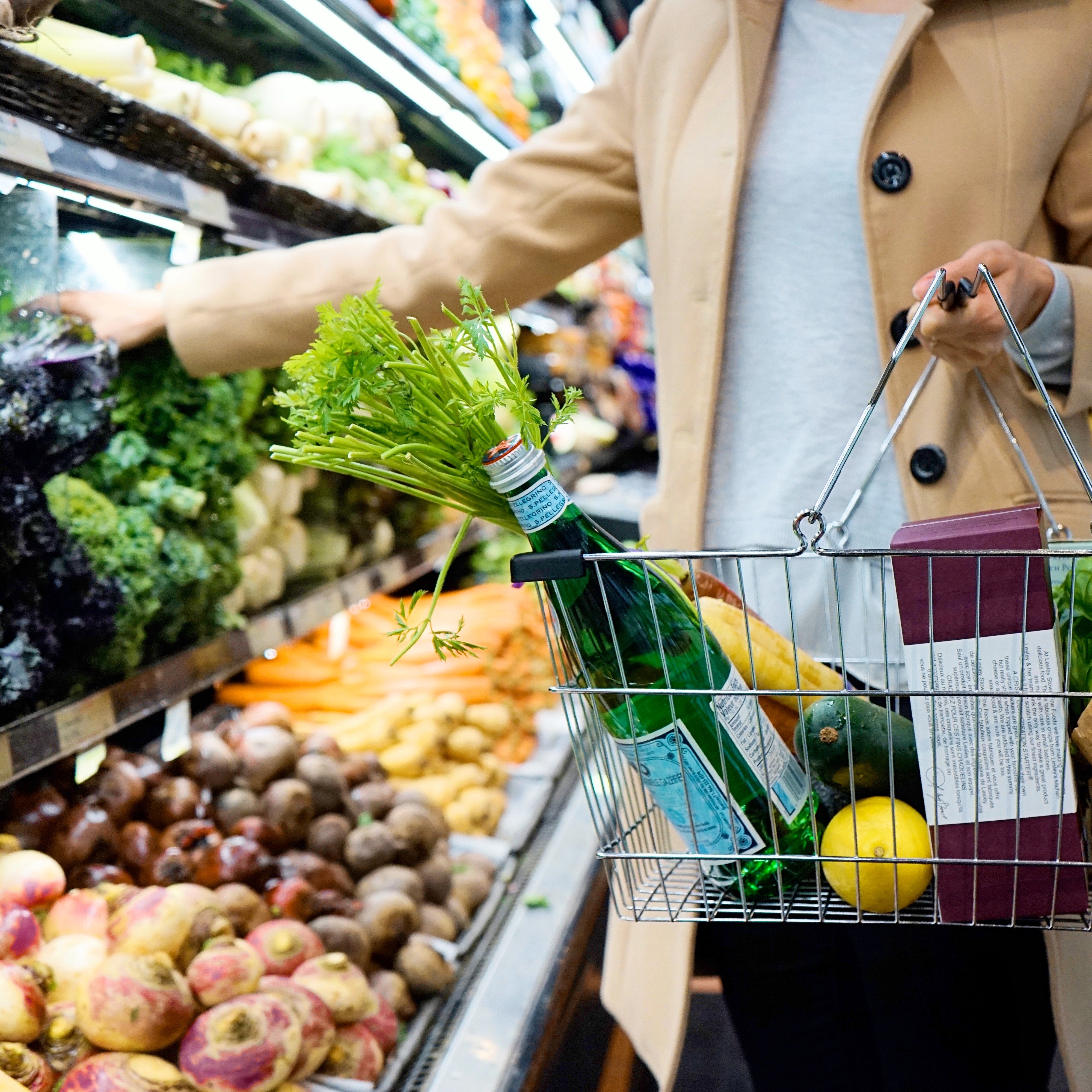 一个人在澳大利亚杂货店购物，篮子里装满了东西苏打水、水果和蔬菜。